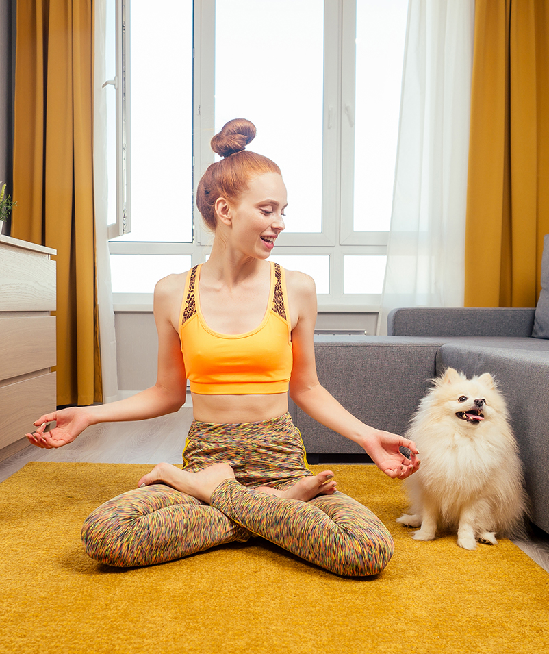 Woman doing Yoga in home with dog companion